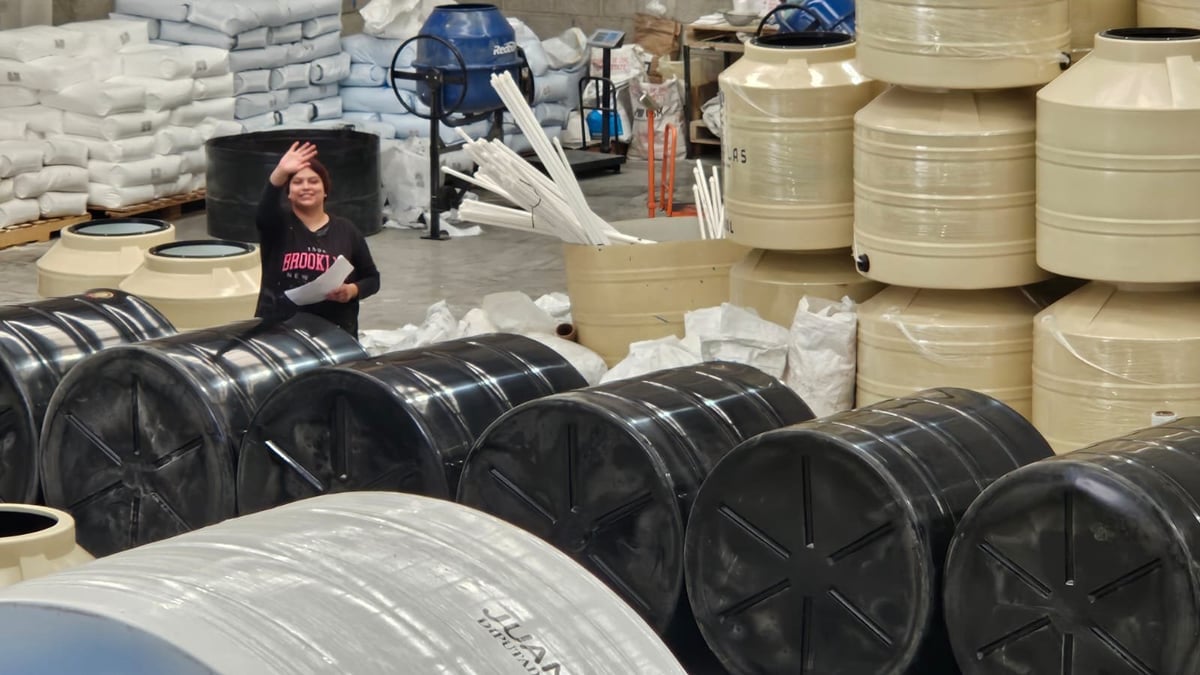 Industrial warehouse worker standing among large black coils and tan storage tanks for manufacturing equipment