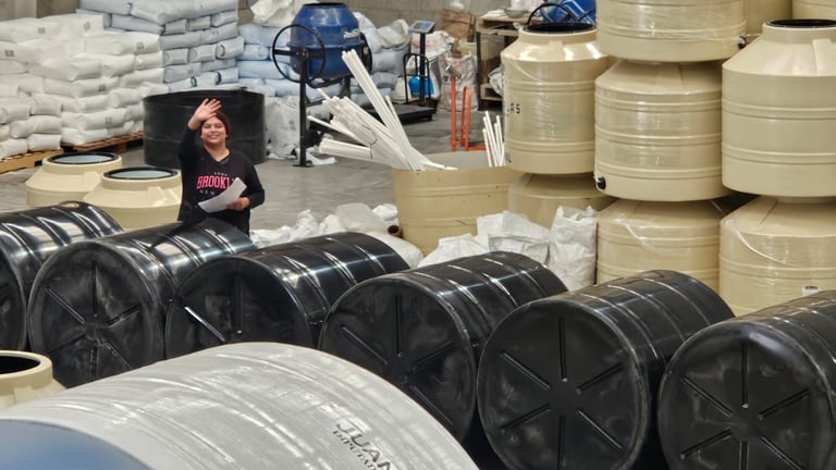 Industrial warehouse worker standing among large black coils and tan storage tanks for manufacturing equipment