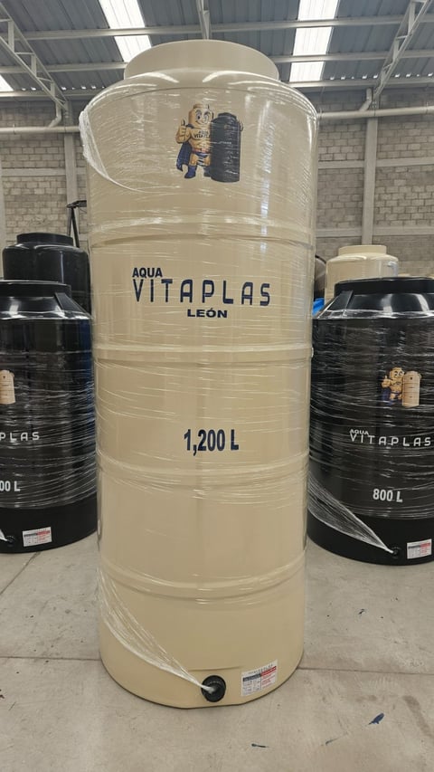 Large cream-colored Aqua Vitaplas water storage tank labeled 1,200L in warehouse with black tanks nearby