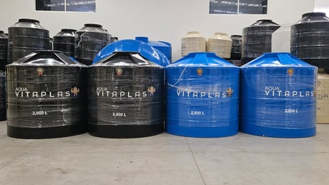 Row of plastic water storage tanks in black and blue colors labeled Vitaplas displayed on warehouse floor
