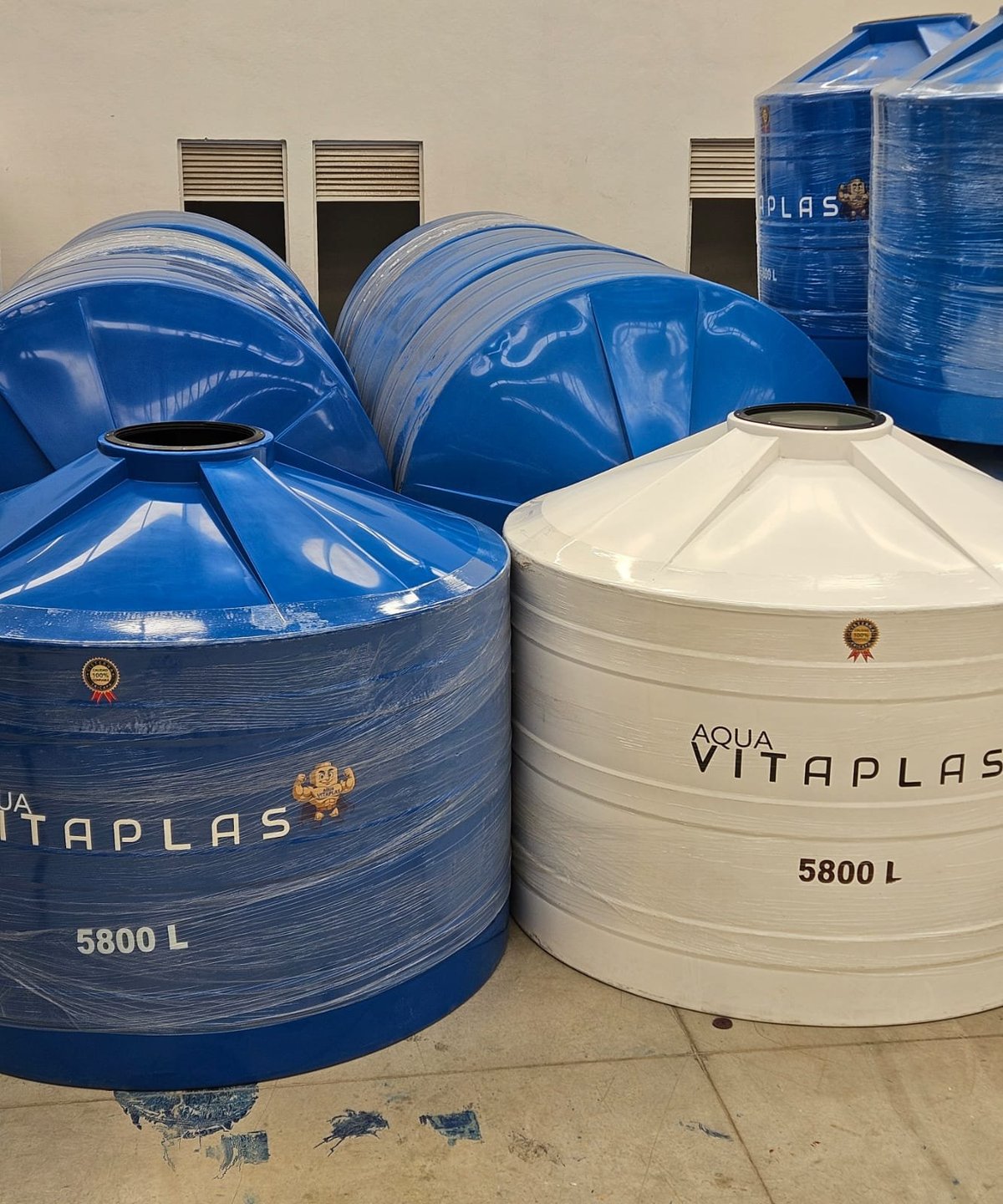Blue and white Aqua Vitaplas water storage tanks with 5800L capacity displayed in rows against a wall