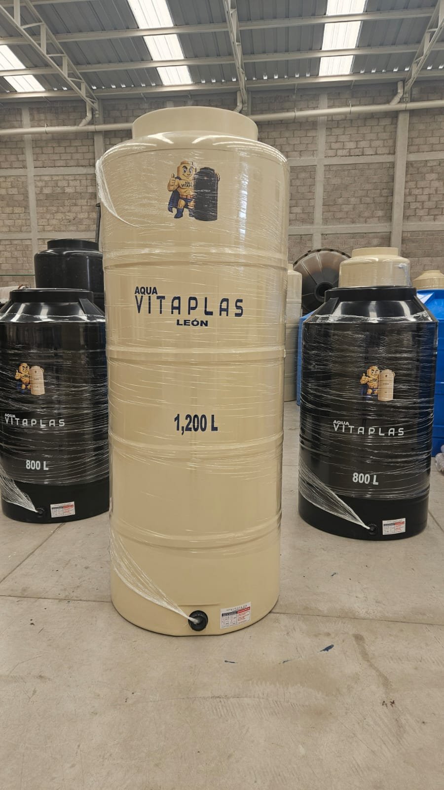 Large cream-colored Vitaplas water storage tank with 1,200 liter capacity flanked by two black 800-liter tanks in warehouse
